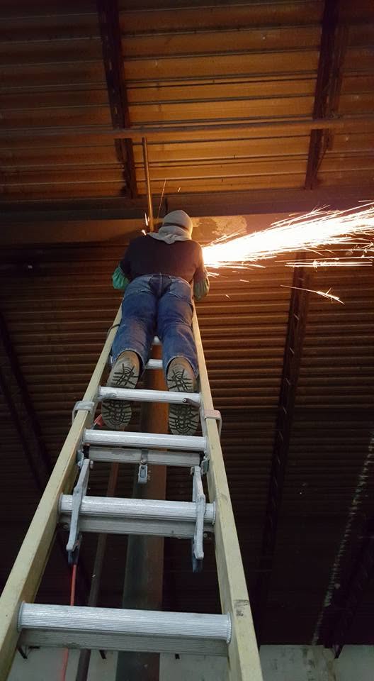 Welder making overhead structural repair with sparks flying inside a commercial building